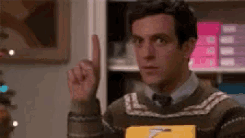 a man in a sweater and tie is pointing up while holding a box .