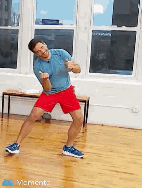 a man in a blue shirt and red shorts is dancing on a wooden floor with the word momento below him