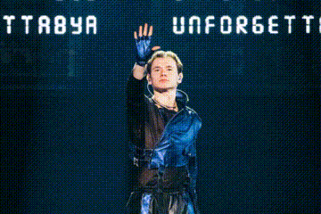 a man stands in front of a sign that says tta8ya unforgettable