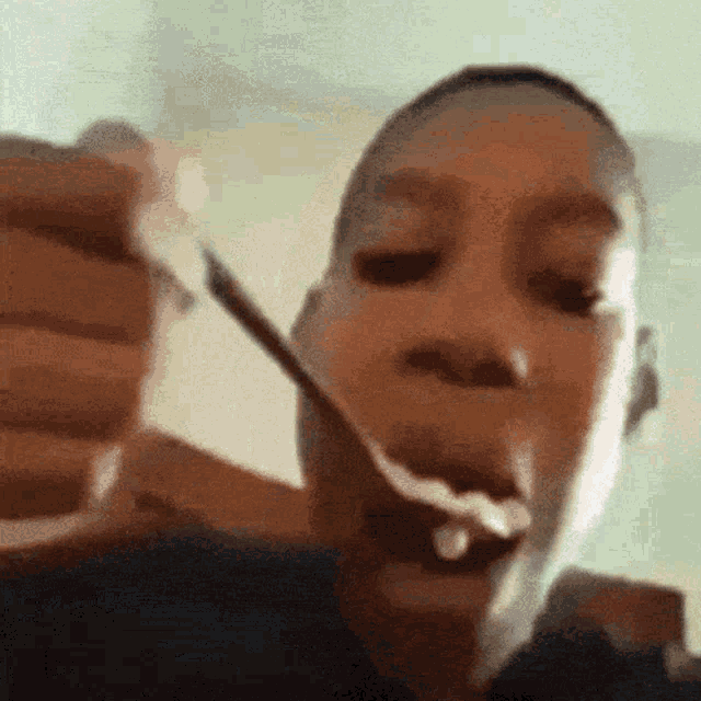 a young boy is eating food with a spoon in his mouth .