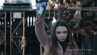 a girl in a pink jacket holds up a blue bottle in front of a building