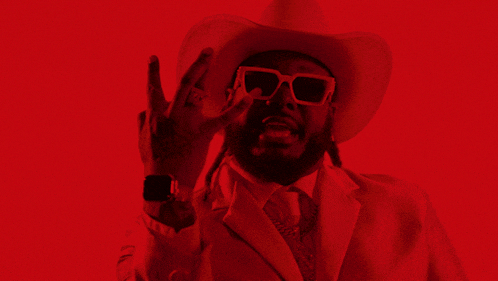 a man wearing a cowboy hat and sunglasses shows off his watch