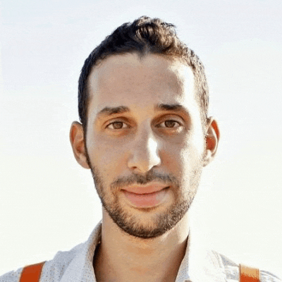 a man with a beard wearing a white shirt and orange suspenders is smiling for the camera .