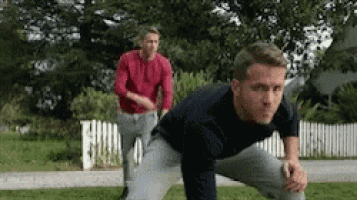 a man in a black shirt is stretching his legs while another man in a red shirt is running behind him .