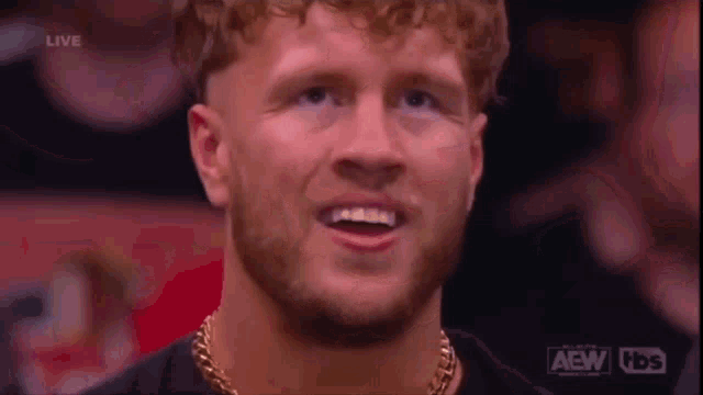 a man with a beard is wearing a gold chain around his neck and smiling at the camera .