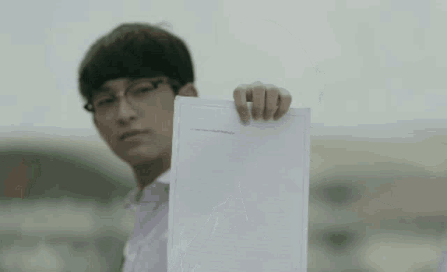 a young man in a white shirt is talking to another man while holding a piece of paper .