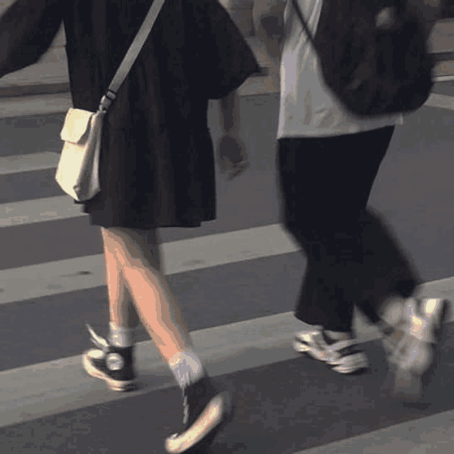 a man and a woman are walking across a street holding hands .