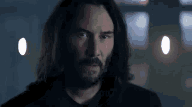a man with long hair and a beard is standing in a dark room .