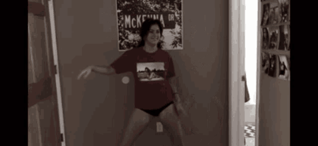 a woman in a red shirt is dancing in a room with a poster on the wall that says mcke