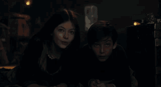 a boy and a girl are laying on the floor in a dark room looking at something .