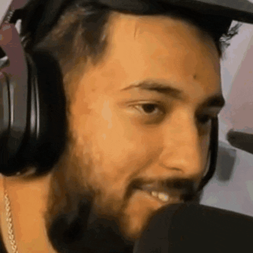 a man with a beard wearing headphones and a hat is smiling into a microphone .