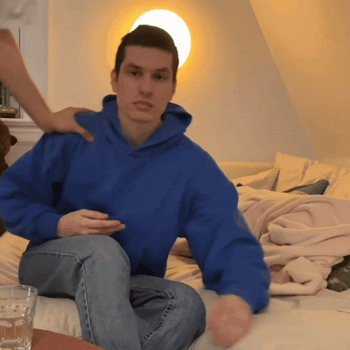 a man in a blue hoodie sits on a couch