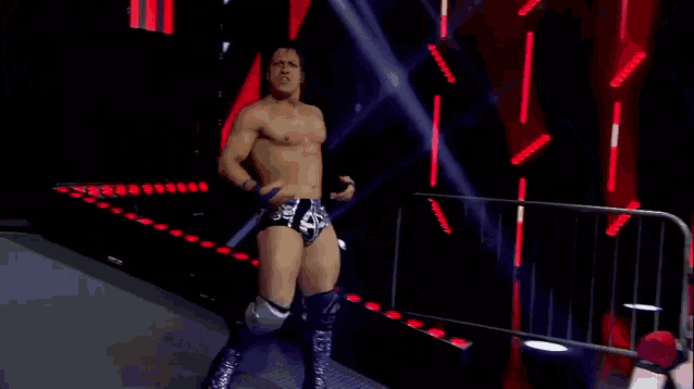 a wrestler without a shirt is standing on a stage with his arms outstretched