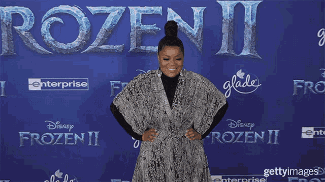 a woman stands on a blue carpet in front of a disney frozen ii poster