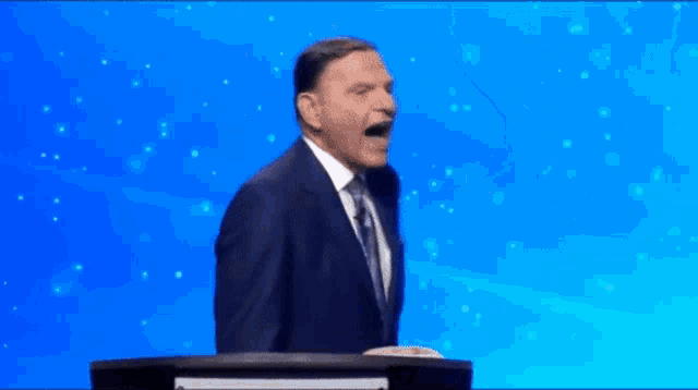 a man in a suit and tie is standing at a podium with his mouth open