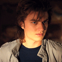 a young man wearing a grey jacket and a blue shirt looks at the camera