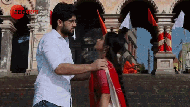 a man and woman are kissing in front of a building with a red circle that says zee