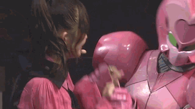a woman in a pink dress is standing next to a robot in a pink suit .