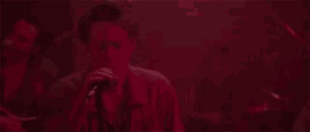 a man is singing into a microphone in a dark room with red lights .