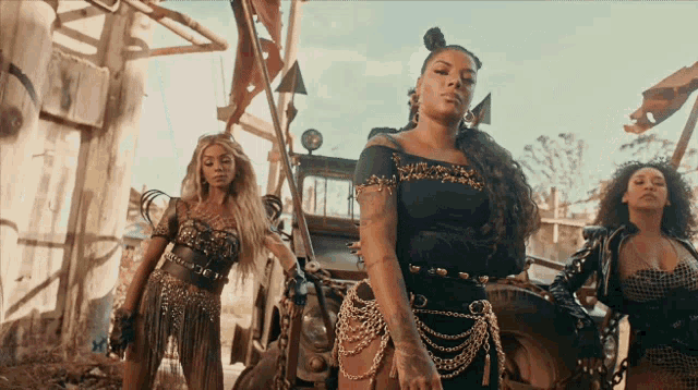 a woman in a black dress with gold chains around her waist is standing next to two other women