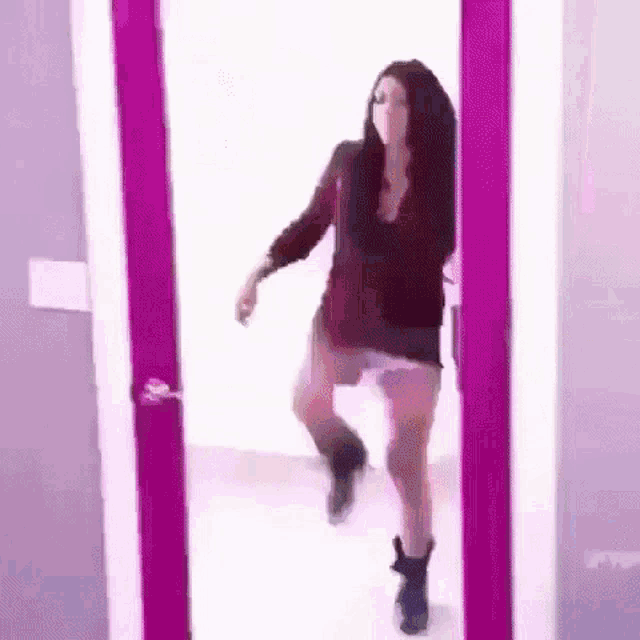 a woman is dancing in front of a mirror in a room with a pink door .