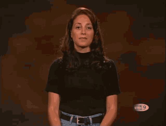 a woman wearing a black shirt and jeans stands in front of a un19 logo