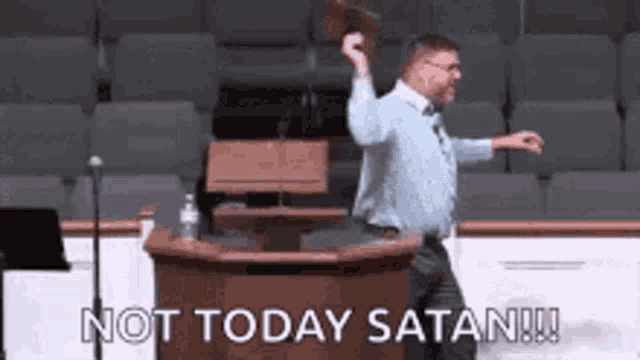 a man is standing in front of a podium holding a bible in his hand and saying not today satan .