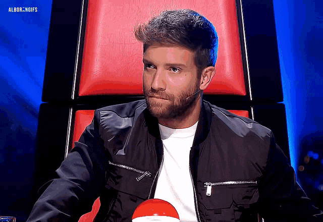 a man in a black jacket sits in a red chair with the words albor.ngifs on the bottom