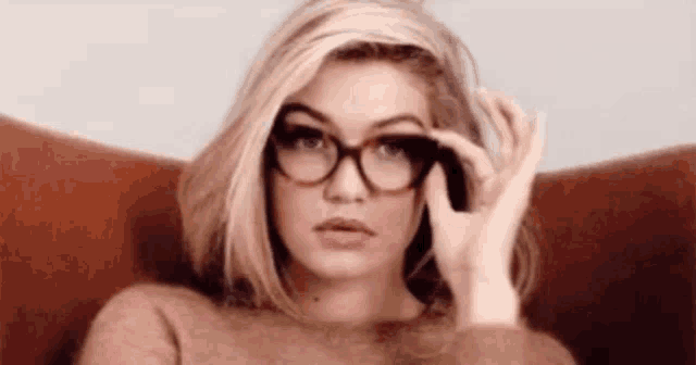 a woman is sitting in a chair wearing glasses and a sweater .