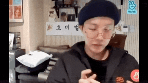a man wearing glasses and a hat is sitting in a room with a sign that says vlive .
