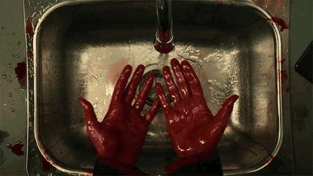 a person washing their hands in a sink with red paint on them
