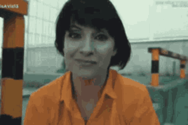 a woman in an orange shirt is smiling in front of a building .