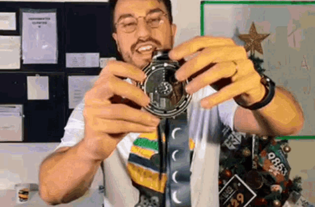 a man wearing glasses is holding a watch in front of a christmas tree ..
