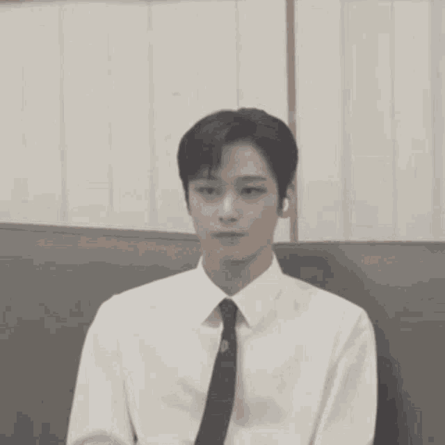 a young man wearing a white shirt and tie is sitting on a couch .