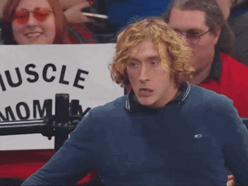 a man in a blue shirt stands in front of a sign that says muscle mom