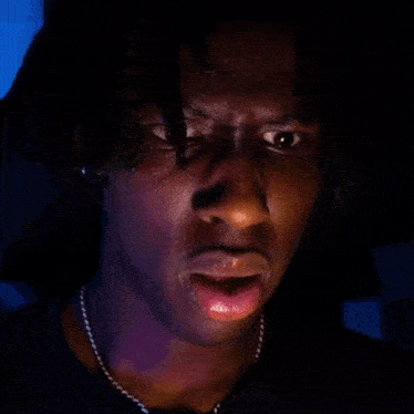 a man with dreadlocks and a necklace is making a funny face in the dark .