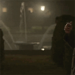 a man is standing in front of a fountain at night holding a cigarette .