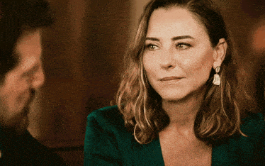 a woman wearing a green shirt and earrings looks at a man