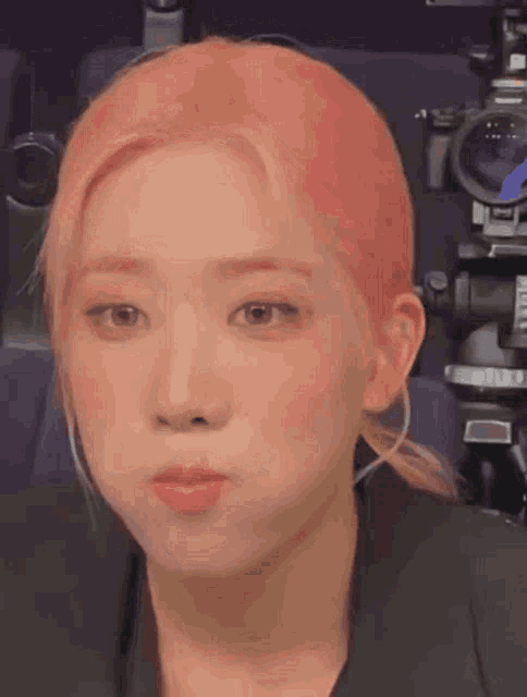 a close up of a woman with pink hair making a face in front of a camera .