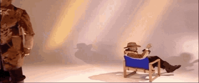 a man in a cowboy hat is sitting in a blue chair while another man stands behind him .