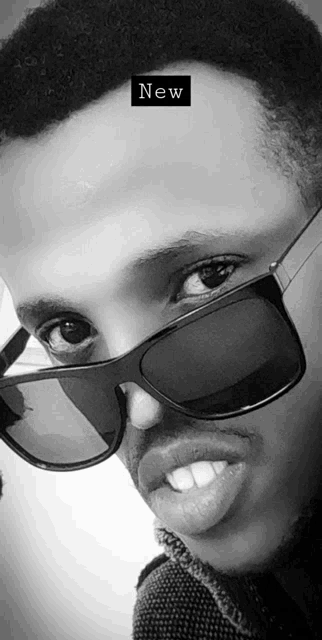 a black and white photo of a man wearing sunglasses with a new sticker on his head