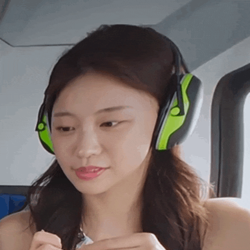 a woman wearing green and black ear muffs looks at her phone