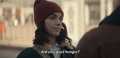 a woman wearing a red hat is talking to a man and says are you guys hungry ?