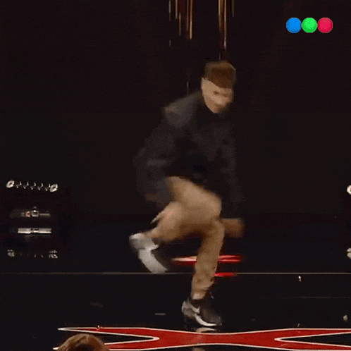a man is dancing on a stage with a red x in the middle
