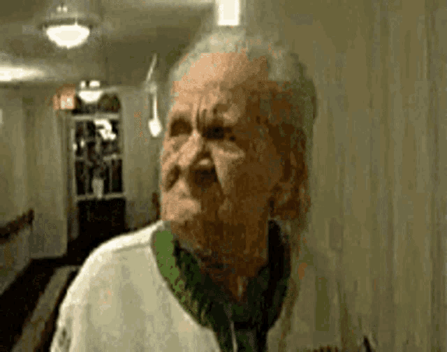 an elderly woman wearing a green sweater is making a funny face in a hallway