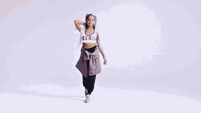 ariana grande is wearing a purple jacket tied around her waist and a crop top .