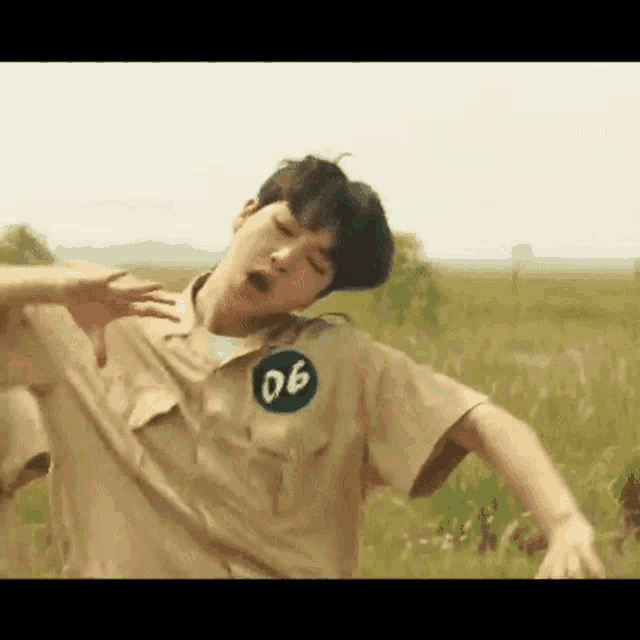 a young man in a khaki shirt is standing in a field .