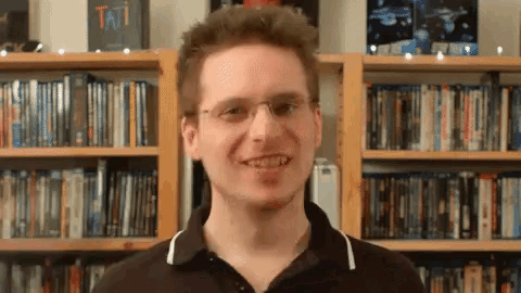 a man stands in front of a bookshelf with a book titled tati in the background