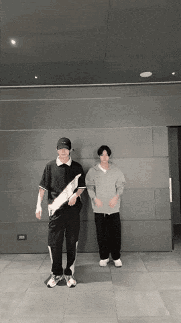 two young men are standing next to each other in front of a wall .