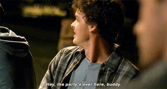 a man in a plaid shirt is talking to another man in a dark room .